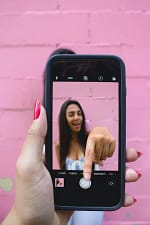 Woman in front of a pink wall filming on her cell phone