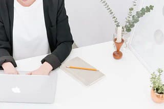 Person working on a MacBook with a notepad and plants nearby.  Engaging Content