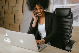 Woman smiling while on the phone looking at her computer wearing a black blazer