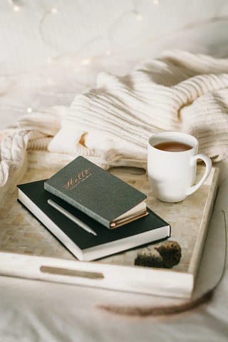 A book, journal, and a cup of coffee on a tray.