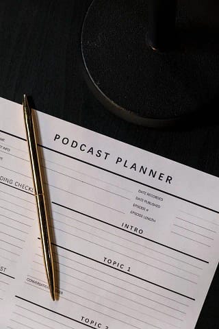 Piece of paper titled Podcast Planner with a gold pen on top of it