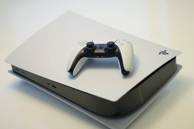 White Playstation 5 laying on it's side with a white playstation controller on top of it.