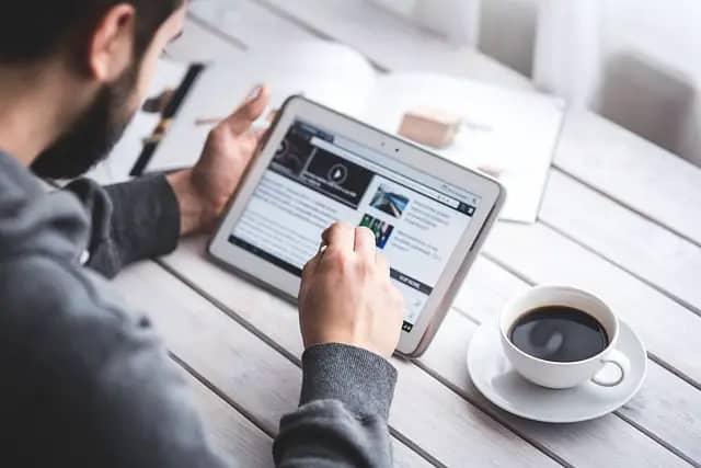 Man using a tablet with a cup of coffee and a notebook next to him